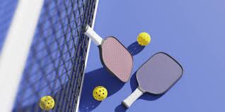 2 pickleball paddles one laying against the net and the other laying on the ground there are 3 pickle balls scattered around the paddles